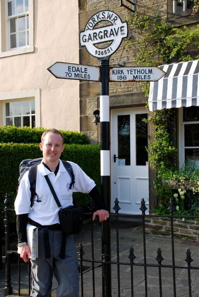 Steve by road sign pointing to Edale and Kirk Yetholm - these distances are for road users. Pennine Way walkers still have over 200 miles to go! Gargrave, Yorkshire