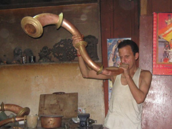 Man demonstrating the copper temple horn he has made