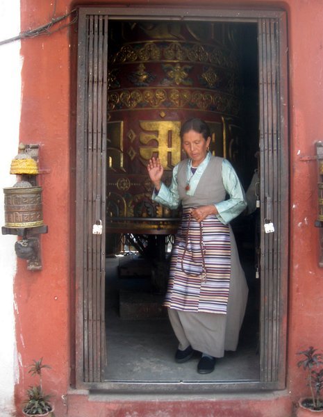 Tibetan lady in traditional dress spinning prayer wheels as she walks the circumference of the Bodhnath Stupa