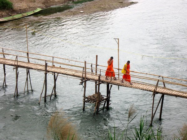 Monks crossing bamboo bridge over river in Luang Prabang