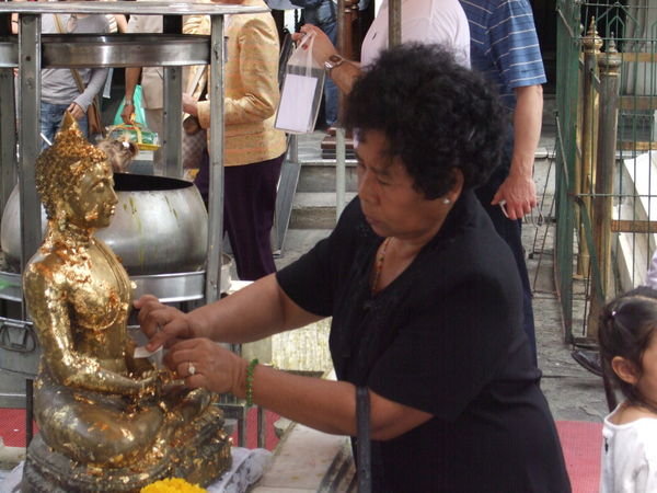 A woman taking a piece of the gold leaf off and making her prayer