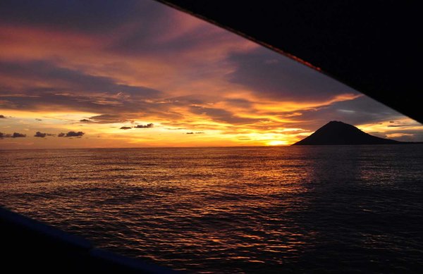 The Sun sets over Manado Dua, as we sail out to Siladen