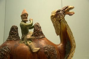 Polychrome-glazed pottery figurine of man blowing instrument on camel