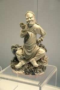 Underglaze blue statue of man blowing a conch on an animal