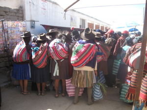 A group of Bolivians typically dressed crowding round a stall