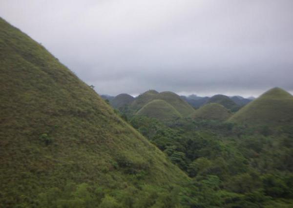 Green icing covered Chocolate Hills on a cloudy day
