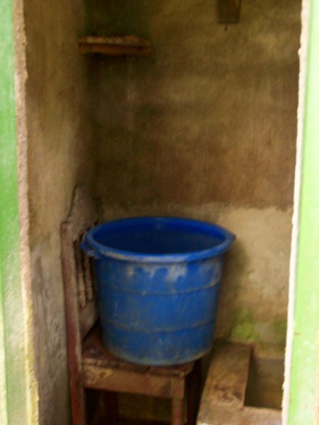 inside of bano.  big bucket on chair, cistern to the right, small bucket inside of big bucket