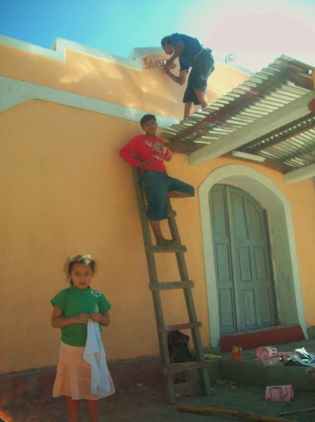 chema painting, helped by geovani, and watched by febe, daughter of the pastor