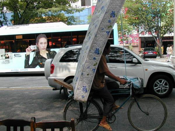 Man carrying mattress on bicycle