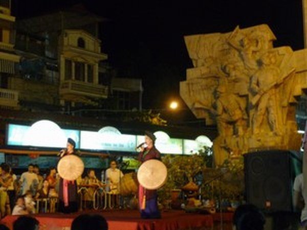 Woman singing at a Market with a huge Communist-looking statue behind her
