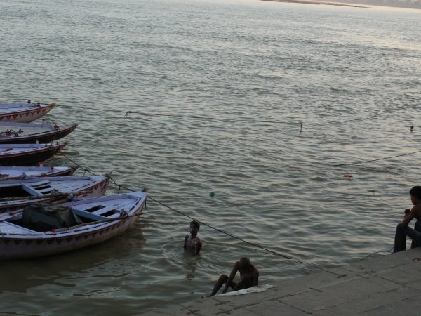 Barquitas esperando pasajeros y gente banandose en el sagrado Ganges