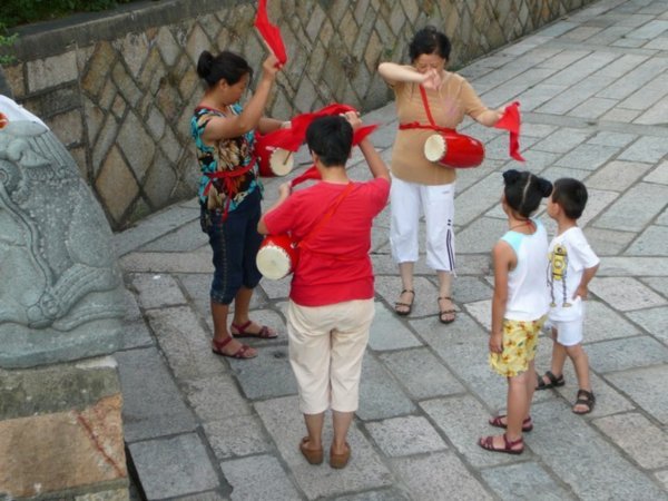Aan de voet van deze pagode oefenen vrouwen simultaan percussie en vlaggenzwaaien onder belangstelling van de plaatselijke jeugd en niet zo plaatselijke fotografen.