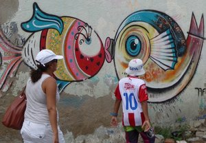 Patricia en Anuar lopen langs kleurrijke muurschilderingen.