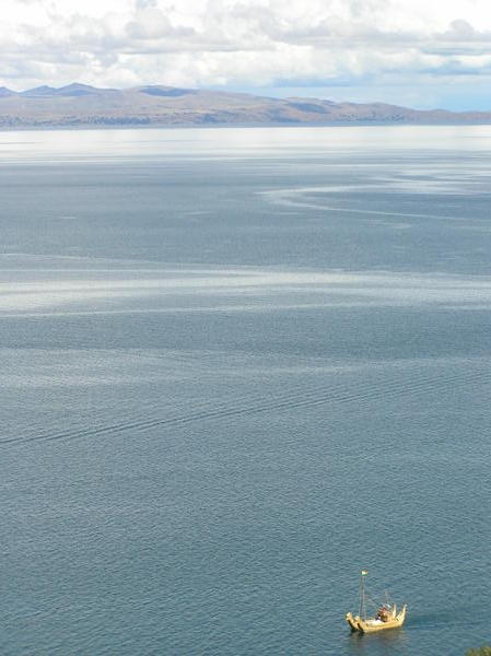 A traditional grass reed boat as seen from the summit of the island. Shore of Lake Titicaca in the background