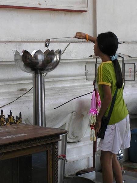 Girl obtaining cupful of holy water to pour over Buddha
