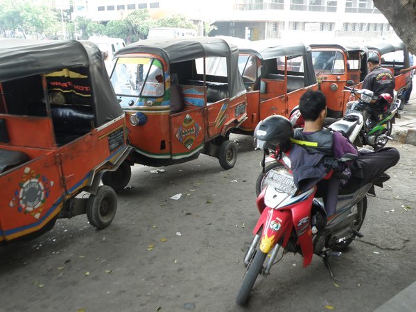 A stream of Bajaj (3 wheel cabs) and an Opelet (motorbike cab)