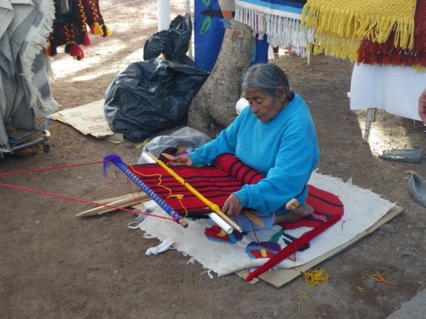 Woman weaving a rug beside her vendor stall
