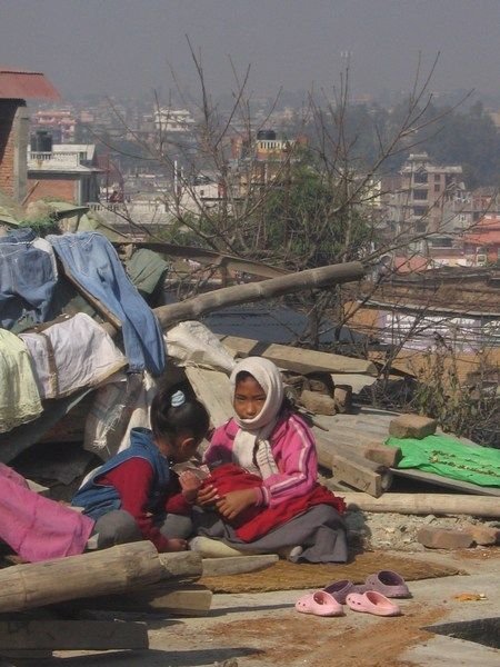 Children sitting on their home's rooftop taking care of the family baby