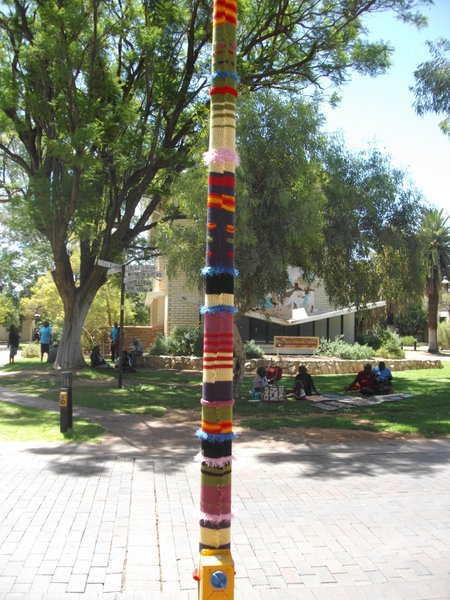 A lamppost wearing a jumper & Aboriginals sitting on the grass